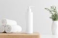 White cosmetic shampoo dispenser bottle mockup with towels and a rosemary on a wooden table