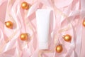 White cosmetic tube, roll pink gold ribbons and golden balls on pink background, mockup. Daily cream, gel, skin care, sunscreen,