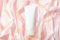 White cosmetic tube, roll pink and gold ribbons on pink background, mockup. Daily cream, gel, skin care, sunscreen, moisturizer.