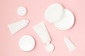 White cosmetic tubes and cream containers top view on pink background