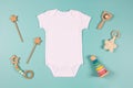 White cotton baby short sleeve bodysuit and natural wooden toy on light blue background. Infant onesie mockup. Blank