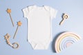 White cotton baby short sleeve bodysuit and natural wooden toys on light green background. Infant onesie mockup. Blank