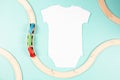 White cotton baby short sleeve bodysuit and wooden toy train on light green background. Infant onesie mockup. Blank