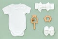 White cotton bodysuit for baby mockup in eco style on a mint green background. Cute booties, headband, wooden rattle and teethers Royalty Free Stock Photo