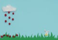 White cotton cloud with the rain of small red Easter eggs falling on green grass and Easter bunny on blue background. Happy Easter
