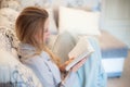 White cozy bed and a beautiful girl, reading a book in the evening, concepts of home and comfort. Close up