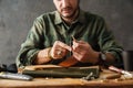 White craftsman sewing while making leather wallet