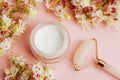 White cream jar and rose quartz facial roller with Horse chestnut flowers on pink background. Natural organic cosmetics