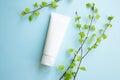 White Cream tube and birch branches with young small leaves on blue background. Cosmetic skincare product blank plastic package. Royalty Free Stock Photo