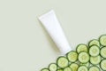 White Cream tube and cucumber slices on light green background. White unbranded lotion, balsam, hand creme, toothpaste mockup.