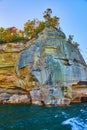 White cresting waves in teal lake waters beneath pictured rocks cliff face with fall trees