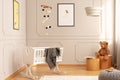 White crib in a cozy toddler room interior with bee posters, teddy bear and lamp.
