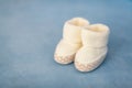 White crochet baby booties on blue background, closeup