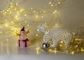 White crocheted deer Rudolph, Santa Claus and various Christmas decorations, illuminated white light chain background, Christmas