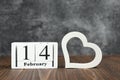 White cube calendar with date of February 14 with heart on wooden background.