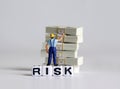 A white cube with `RISK` text. Bundle of $100 bills and a miniature man. Royalty Free Stock Photo