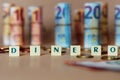 Cubes spelling Dinero in front of Spanish dinero bills and coins on the table Royalty Free Stock Photo