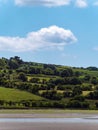 A white cumulus cloud in a blue sky. Trees on the slope of a green hill. Picturesque summer landscape. Irish nature. Green hill