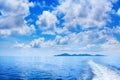 White cumulus clouds in blue sky over sea landscape, many clouds above ocean water panorama, ship trail, island on horizon line Royalty Free Stock Photo