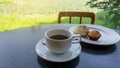 White cup of americano black coffee, cup cake and cereal bread on white plate on black table, green landscape on background under Royalty Free Stock Photo