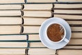 A white cup of aromatic coffee against the background of worn out old books folded upside down