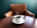 White cup of black coffee on brown wood table with cozy armchair Royalty Free Stock Photo