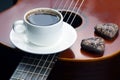 the white cup with black coffee and cookies lying on the acoustic guitar