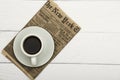 White cup with black coffee and old newspaper on a white woody background. Coffee on a white woody background. View from above. Pl