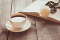 White cup of black coffee and open book with white rose on wooden board. Vintage. Close up. Royalty Free Stock Photo