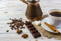 A white cup with black coffee on sacking, anise, sugar, a piece of chocolate, coffee beans and cinnamon sticks on bright wooden ta Royalty Free Stock Photo