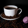 A white cup with black fragrant coffee stands on a black background with coffee zurnes next to colorful french cookies macaroons Royalty Free Stock Photo