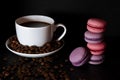 A white cup with black fragrant coffee stands on a black background with coffee zurnes next to colorful french cookies macaroons Royalty Free Stock Photo