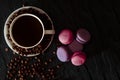 A white cup with black fragrant coffee stands on a black background with coffee zurnes next to colorful french cookies macaroons Royalty Free Stock Photo