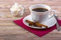 White cup of black hot coffee on saucer, served with white sugar cubes in a bowl, tea spoon, anise and cinnamon sticks on wooden t Royalty Free Stock Photo