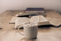 White cup with cappuccino coffee accompanied by a series of books on a rustic   table Royalty Free Stock Photo