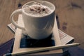 White cup with cappuccino coffee on top of a small tower  of books inside a hipster room Royalty Free Stock Photo