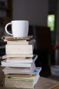 cup with cappuccino coffee on top of a small tower made up of books inside a hipster room