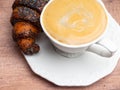 White cup of cappuccino, fresh croissant on wooden table. Latte, macro, top view