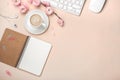 White cup with cappuccino, sakura flowers, keyboard, alarm clock, notebook on a pastel pink background