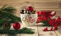 White cup with Christmas balls, natural pine branches and red ilex berries around. Winter still life with gift red box Royalty Free Stock Photo