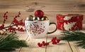 White cup with Christmas balls, natural pine branches and red ilex berries around. Winter still life with gift red box Royalty Free Stock Photo