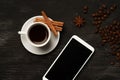 White cup with cinnamon and anise coffee sticks and a mobile phone with a blank screen on a black background with coffee beans and Royalty Free Stock Photo