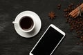 White cup with cinnamon and anise coffee sticks and a mobile phone with a blank screen on a black background with coffee beans and Royalty Free Stock Photo