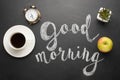 A white cup of coffee with an alarm clock and an apple and a good morning inscription. Concept of a cheerful and kind morning