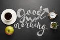 A white cup of coffee with an alarm clock and an apple and a good morning inscription. Concept of a cheerful and kind morning