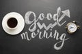 A white cup of coffee with an alarm clock and an inscription good morning. Concept of a cheerful and kind morning