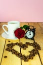 A white cup of coffee, coffee beans, a red rose and an alarm clock on a wooden table. Breakfast. Morning with a cup of coffee. Royalty Free Stock Photo