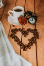 A white cup of coffee, coffee beans, a red rose and an alarm clock on a wooden table. Breakfast. Morning with a cup of coffee. Royalty Free Stock Photo