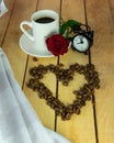 A white cup of coffee, coffee beans, a red rose and an alarm clock on a wooden table. Breakfast. Morning with a cup of coffee. Royalty Free Stock Photo