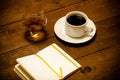 White cup of coffee, cognac in a glass and notebook on old wooden table. Toned